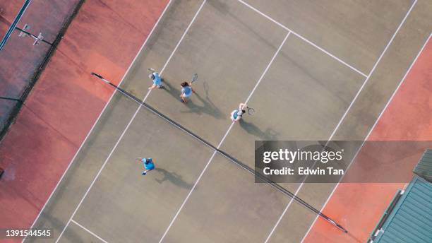 drohnen-standpunkt asiatischer tennislehrer, der seine erwachsenen schüler führt serving the ball - tennis court top view stock-fotos und bilder