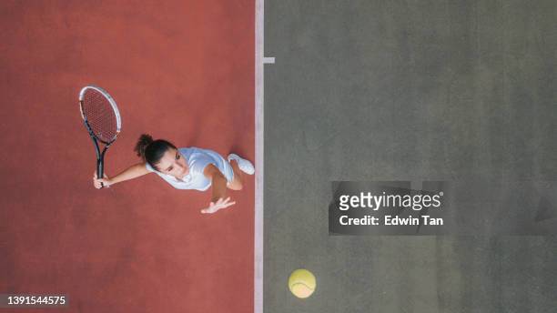 drohnen-sicht weißes teenager-mädchen tennisspielerin serviert den ball beim üben auf dem tennisplatz direkt darüber - schlägersport stock-fotos und bilder