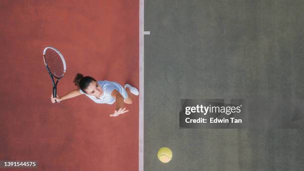 drone point of view white teenage girl tennis player serving the ball practicing at tennis court directly above - serveren sport stockfoto's en -beelden