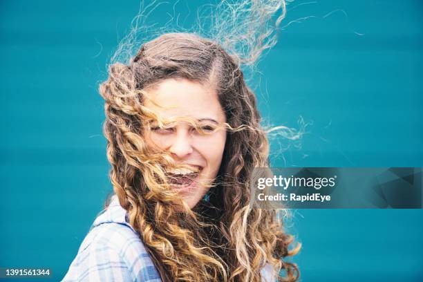 cabello ventoso de día: hermosa joven de cabello rizado se ríe mientras el viento envuelve su largo cabello alrededor de su cara - cabello desmelenado fotografías e imágenes de stock