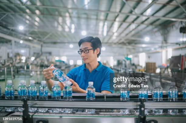asian chinese male production line worker examining water bottle in bottling plant mineral water drinking water factory - bottling plant stock pictures, royalty-free photos & images