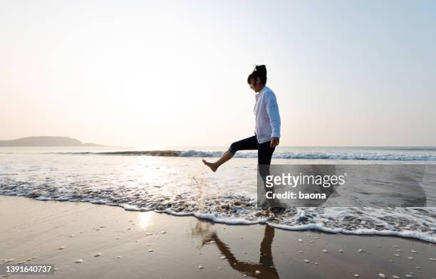 woman kicking waves on water's edge - sand trap stockfoto's en -beelden