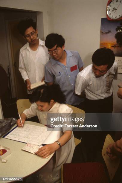 View of a trio of men as they look over the shoulder of a seated census taker who writes in an oversized census logbook, Beijing, China, October 1990.