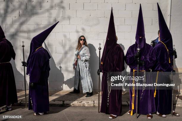 Woman walks next to penitents from the 'Nuestro Padre Jesus Nazareno' brotherhood during 'Las Caidas' procession on Good Friday on April 15, 2022 in...