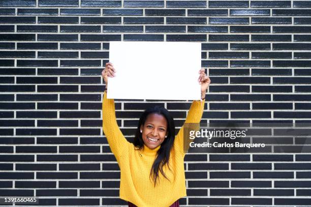 african american young woman holding a blank banner - help wanted sign photos et images de collection