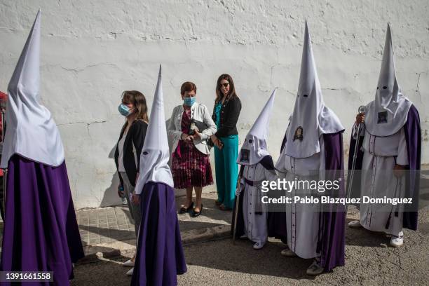 Women stand next to penitents from the 'Santa Mujer Veronica' brotherhood during 'Las Caidas' procession on Good Friday on April 15, 2022 in Ocana,...