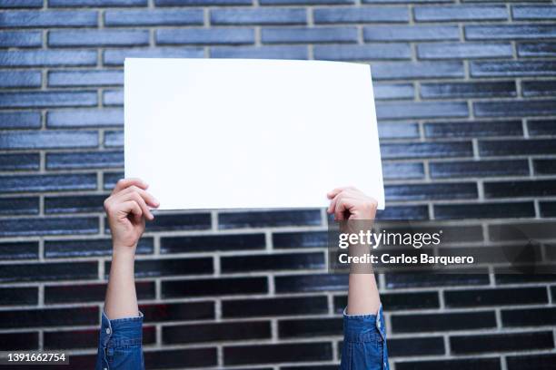 a caucasian man holding a white and empty placard outside, protest banner to be filled with a dark background. - person holding blank sign fotografías e imágenes de stock