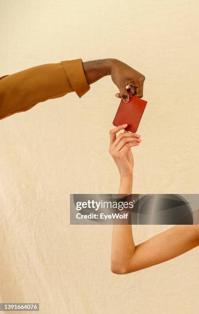 a man's hand passing a wallet to a woman's hand, against a neutral brown background. - cremefarbig stock-fotos und bilder