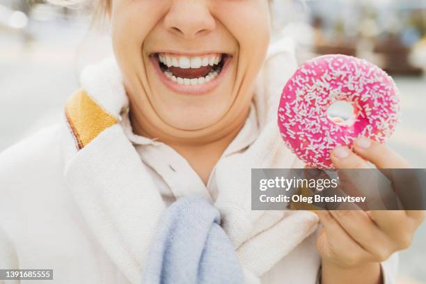 overweight woman with double chin toothy smiling and holding donut. unhealthy fat food concept. unrecognizable person - double chin stock-fotos und bilder