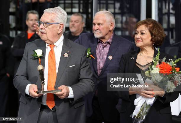 Lou Nolan, the public address announcer of the Philadelphia Flyers, holds a golden microphone with wife Ellen and Bernie Parent during a pregame...