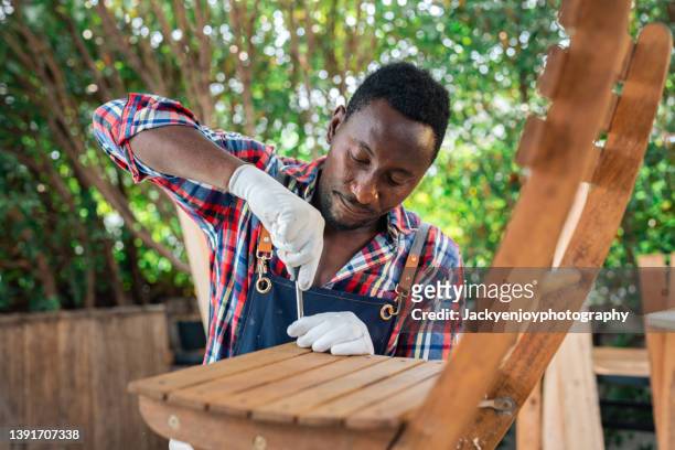 professional carpenter assembling wooden adirondack chair with screwdriver. manual work and do-it-yourself - adirondack chair closeup stock pictures, royalty-free photos & images