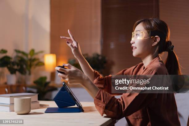 young woman sitting in living room using vr glasses playing video game and working late night at home - overtime sport stock pictures, royalty-free photos & images