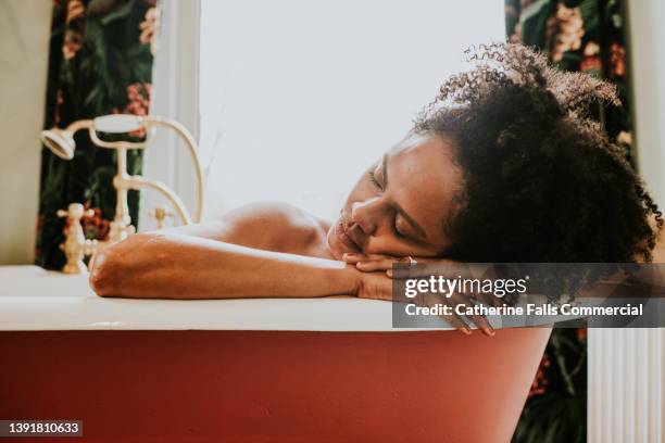 dreamy scene of a beautiful woman resting her head on her arms on the side of a roll top bathtub in a luxurious bathroom - loslassen aktivitäten und sport stock-fotos und bilder