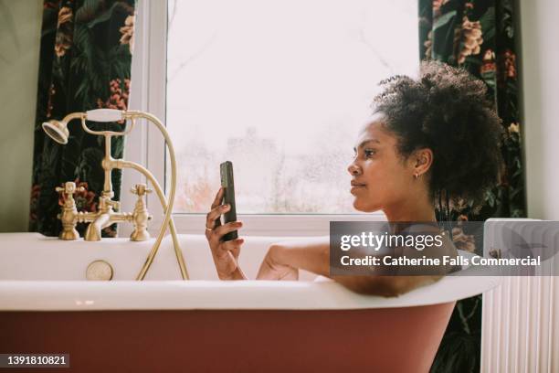 a woman uses a mobile phone while relaxing in a bath - designer bath stock pictures, royalty-free photos & images