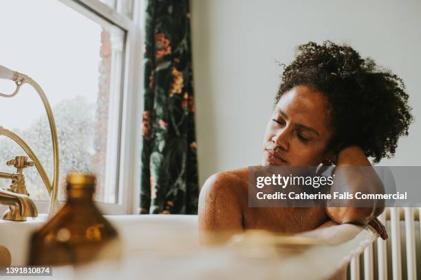 dreamy scene of a beautiful woman bathing in a roll top bathtub in a luxurious bathroom - good condition stock pictures, royalty-free photos & images