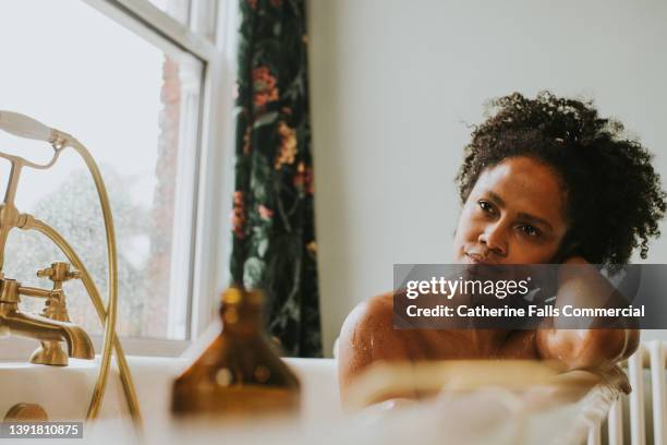 a content, beautiful woman daydreams in a roll top bathtub - bathroom exercise stock pictures, royalty-free photos & images