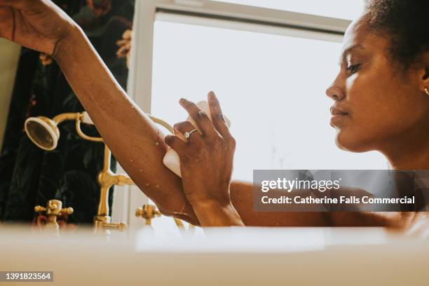 close-up of an elegant woman washing her arm with a bar of soap in the bath - barbade stock-fotos und bilder