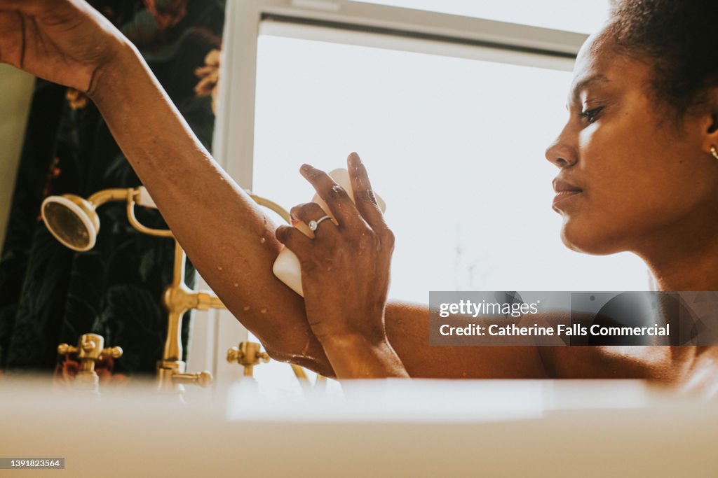 Close-up of an elegant woman washing her arm with a bar of soap in the bath