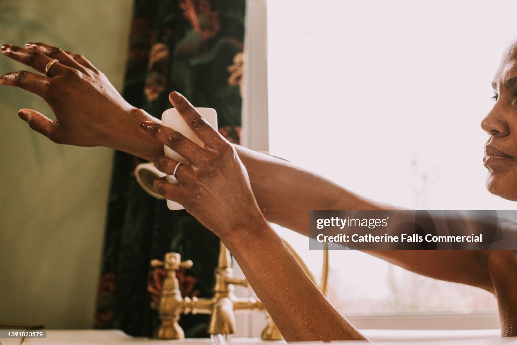Close-up of an elegant woman washing her arm with a bar of soap in the bath