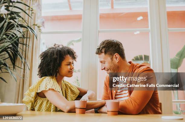 a beautiful young couple looks very much in love as they sit at a dining table sipping hot drinks and flirt. - kantoorromance stockfoto's en -beelden