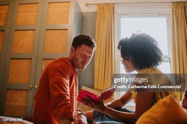 a woman shares a moment with her partner, showing him a section of her book - book discussion stock pictures, royalty-free photos & images