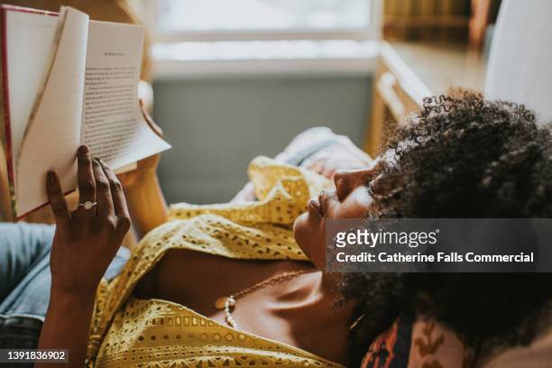 a content woman reclines on a comfortable bed and gets lost in a good book - sfogliare libro foto e immagini stock