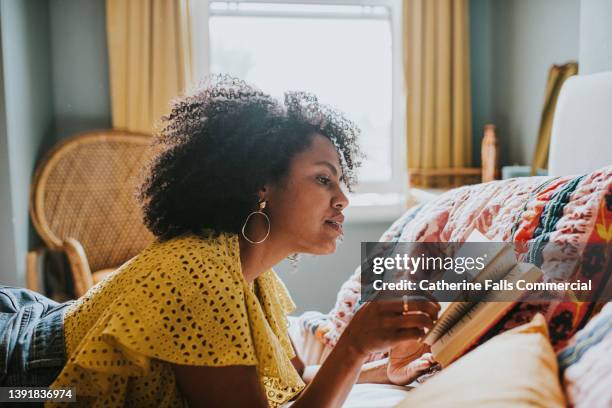 a woman lies on her stomach on a comfortable bed and reads a book - 讀 個照片及圖片檔