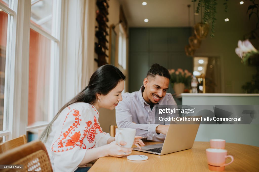 A man and a woman sit at a table, behind a laptop and have a discussion
