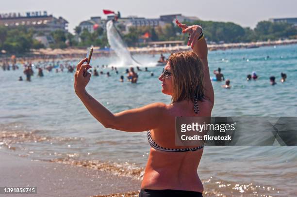 on the beach, an animator celebrates with a flyboard by unfurling the turkish flag on victory day, while a woman takes a selfie. - 29 ekim stock pictures, royalty-free photos & images