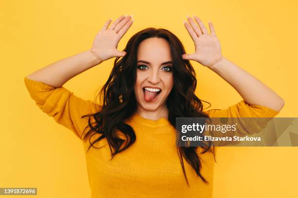 smiling happy curly-haired young woman in a yellow sweater having fun is surprised looking at the camera standing on a yellow isolated background. place for text - a fool stock pictures, royalty-free photos & images