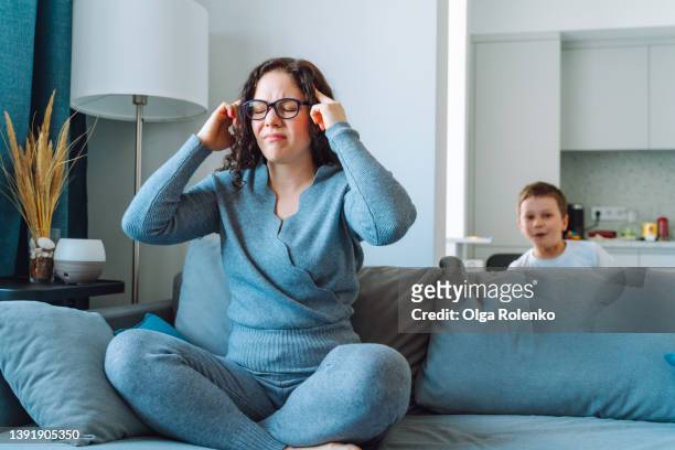 middle age woman in home wear and glasses hold head feeling headache - midlife crisis stock pictures, royalty-free photos & images