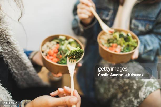 two females friends eating take away vegetarian bowls outdoors in town. - salad to go stock pictures, royalty-free photos & images