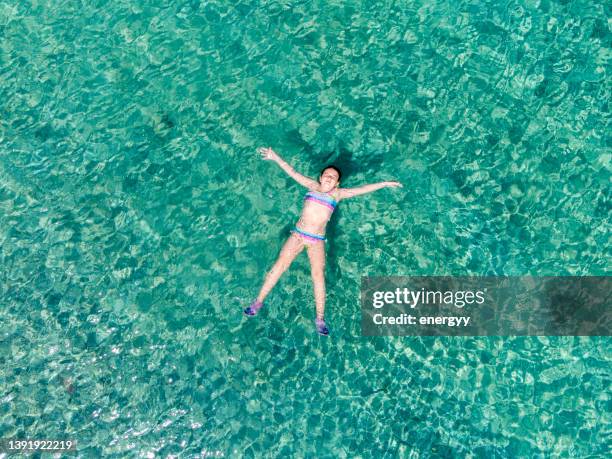 vue aérienne panoramique d’une petite fille flottant sur la mer - ado en maillot de bain photos et images de collection