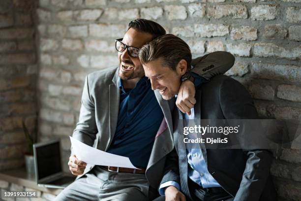 due uomini d'affari felici che ridono insieme in ufficio dopo aver visto grandi risultati. - embracing foto e immagini stock