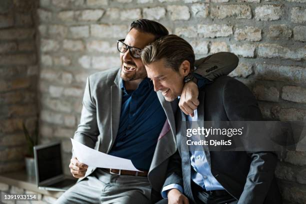 two happy businessmen laughing together in office after seeing great results. - men hugging stock pictures, royalty-free photos & images