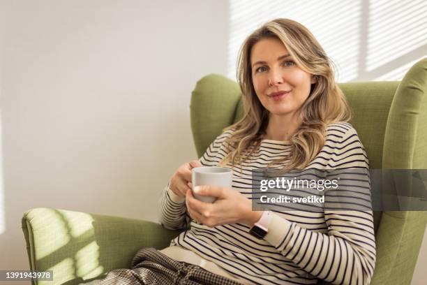 woman drinking coffee at home - armstoel stockfoto's en -beelden