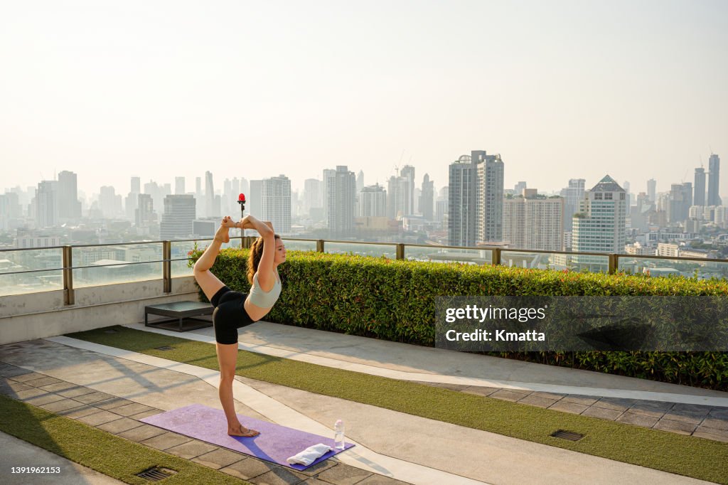 Woman doing yoga on urban rooftop at sunset.