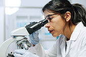Side view of young female biochemist looking in microscope during research