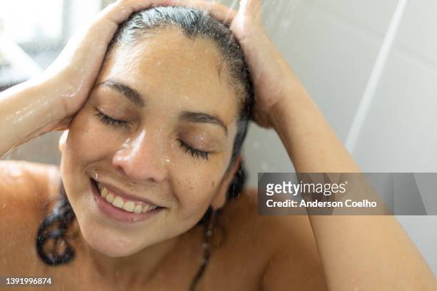 latin woman over 30 smiling taking a hot shower in the bathroom at her home. - women taking showers stock pictures, royalty-free photos & images