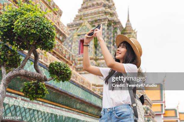 cheerful young asian woman taking photo by smartphone while traveling at wat pho temple in bangkok, thailand. - local landmark stockfoto's en -beelden