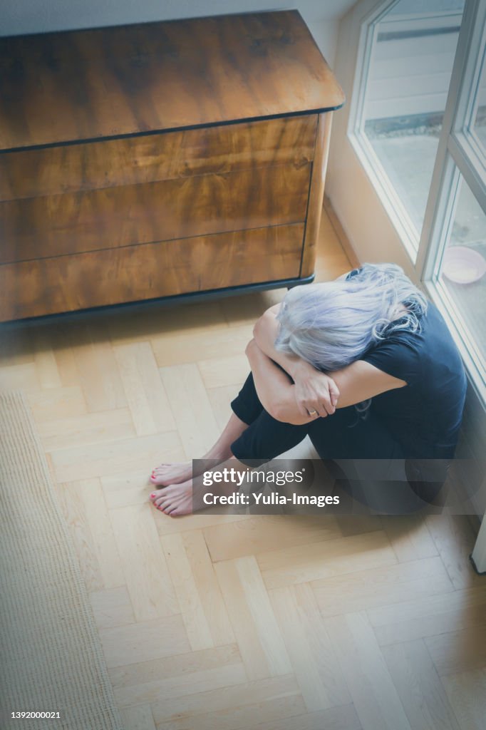 Upset senior woman sitting with head in knees