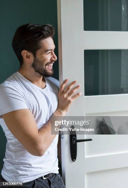 handsome man standing with arms crossed by door against green wall - apartment entry stock pictures, royalty-free photos & images