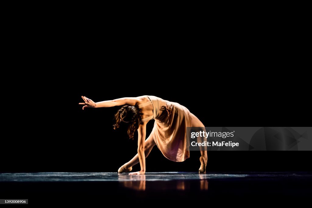 Teenager-Mädchen, das zeitgenössischen Tanz auf dunkler Bühne aufführt