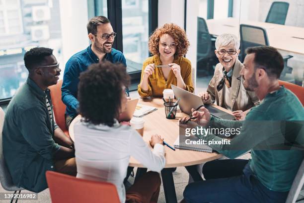 gruppo misto di uomini d'affari seduti attorno a un tavolo e che parlano - coinvolgimento dei dipendenti foto e immagini stock