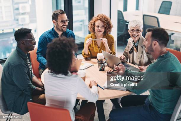 mixed group of business people sitting around a table and talking - business office stock pictures, royalty-free photos & images