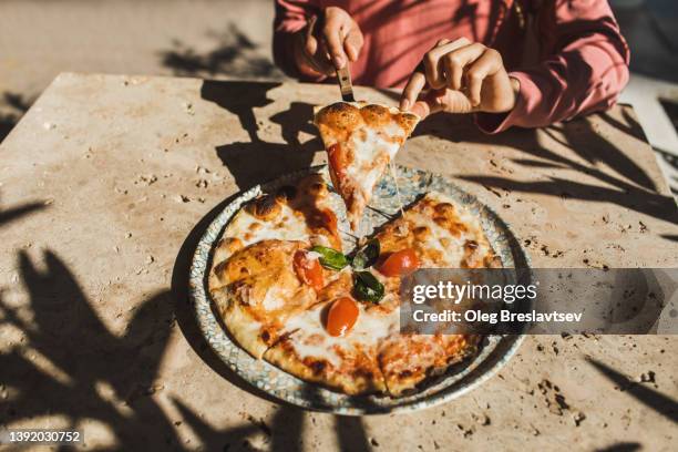 top view of woman hands getting a slice of freshly made pizza. enjoying meal in outdoor restaurant. italian cuisine and culture - pizza margherita stockfoto's en -beelden