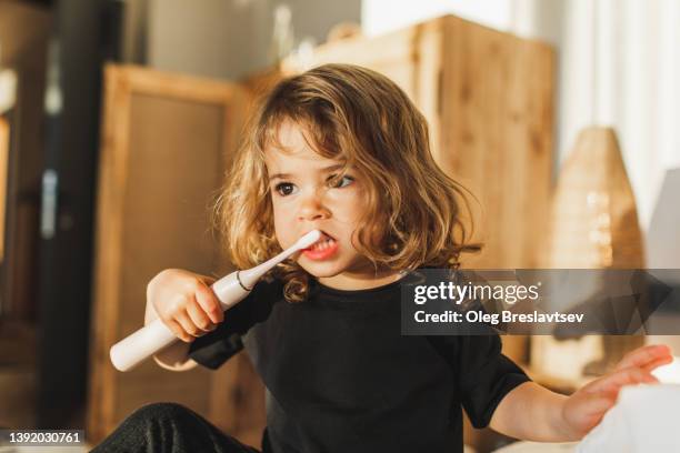 cute baby girl take mom's electric toothbrush and learning to brush her teeth. funny childhood - zähne putzen stock-fotos und bilder