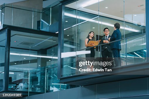 Office building exterior looking through window chinese business person meeting working late at night in meeting room Office building exterior looking through window chinese business person meeting working late at night in meeting room