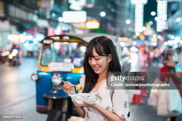 a young asian woman trying some food at night market in bangkok - travel market asia stock-fotos und bilder