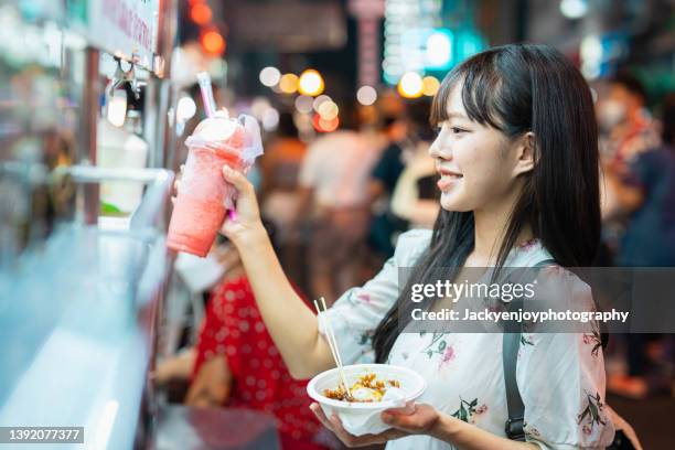 a young smily woman holding fresh juice at food truck in busy night market in bangkok - daily life in bangkok stock-fotos und bilder